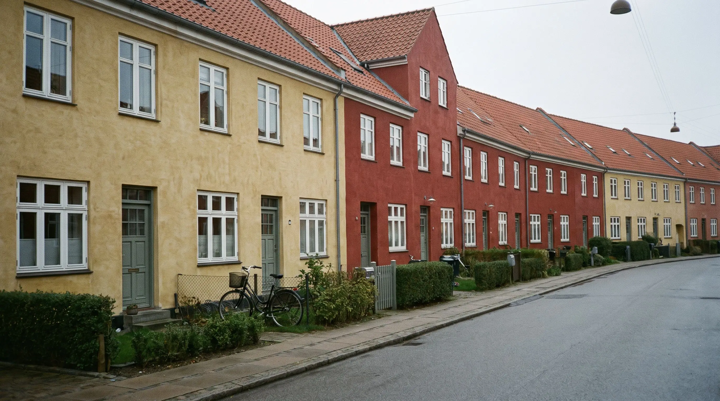 Række af pudsede rækkehuse i gult og rødt i Valby med nymalede hvide vinduer, hække og en cykel ved fortovet